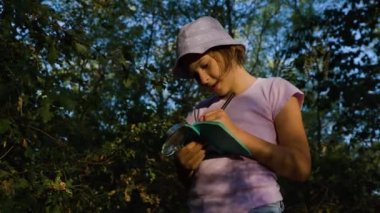Handsome curious kid Naturalist Scientist Explores Plant Life and Insect Life and take notes in his notebook. schoolgirl naturalist studying the leaves in the forest