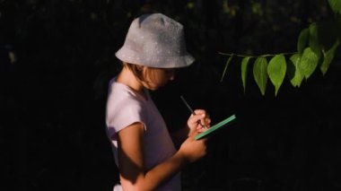 pretty children girl Naturalist Scientist Explores Plant Life and Insect Life take notes in his notebook. Smart Curious kid Botanist and Entomologist Explores Nature.