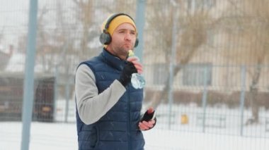 Runner A young and athletic man takes a break from his wintertime run to rehydrate with a drink of water. He is wearing headphones and maintaining his healthy lifestyle even in the cold weather