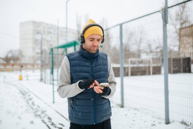 A shot emphasizing the movement and strength of a runner with headphones and smartphone, as he jogs through the winter terrain. showcasing the power and dedication of a dedicated runner.