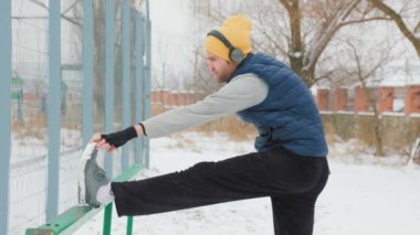 Genç yetişkin bir erkek kış boyunca boş bir aktiviteye katılır, kulaklık takarak dışarıda jimnastiğe katılır..