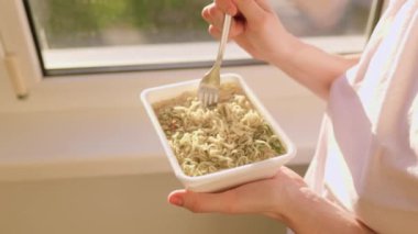 A candid shot of someone enjoying a junk food meal of instant noodles, focuses on the hands and fork, showing the consumption of the unhealthy meal.