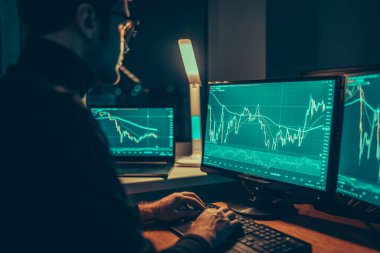 The Analyzer A young adult guy seated at his workstation, surrounded by computer monitors, as he analyzes currency trends and makes trades using calculator