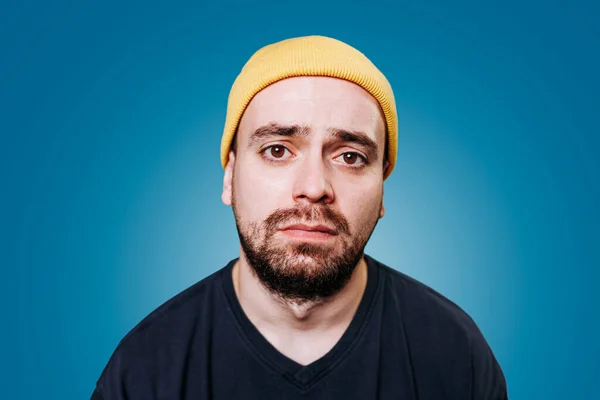 tired, exhausted and unhealthy looking guy, with an unhappy expression, in a studio shot a blue background. looking at the camera, face gaunt, indicating a sense of depression and sadness
