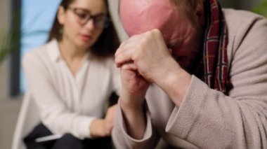 Terapi seansında genç bir psikologla ağlayan bunalımlı yaşlı bir adamın portresi. Genç bir psikoterapist yaşlı bir adama, yaşlı bir adama, bir ilişkiye, bir topluluğa danışıyor.,