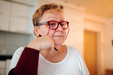Embracing Authenticity This portrait photo captures the essence of a real, overweight woman at home. She is depicted smiling and looking satisfied, wearing glasses and showcasing her blonde hair.