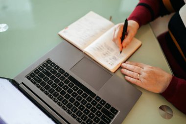 E-Learning by Hand Close-Up of a Woman Writing Notes on a Laptop. This photo highlights the hands of a woman who is actively participating in an online course. The close-up perspective