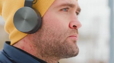 close up of a Young man head having fun while listening music on headphones, with yellow cap, winter time