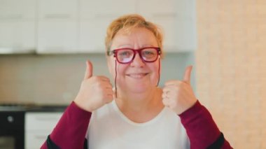 A beaming, overweight elderly woman gives a thumb up and grins from ear to ear in this authentic, real people photo taken at home. With her eyeglasses perched on her head, happiness and satisfaction