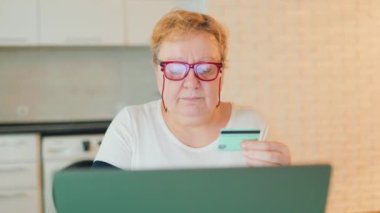 An obese female is making a purchase through an e-commerce platform, using her laptop and credit card. She has her eyeglasses on and is focused on finding the perfect item to buy, shopping at home