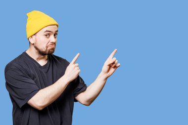 portrait of a handsome and stylish bearded guy in studio shot, grimacing with a bizarre expression while pointing to free space, looking at the camera and providing ample copy space.