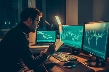 The Night Owl Trader Working late into the night, a man is seen from behind as he analyzes market trends and exchange information in his home office.