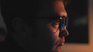 Late Night Analysis A student or professional man, working on his computer in the night time. Close up shot of his determined face, as he invests in the stock market with the help of his glasses.