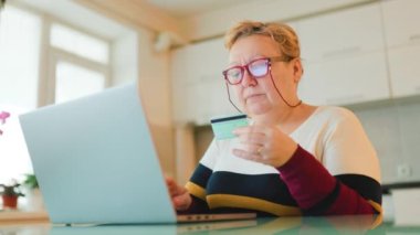 Yaşlı, kilolu bir kadın bilgisayarındaki e-ticaret sitelerine girip kredi kartını alışveriş yapmak için kullanıyor. O rahat bir şekilde evde oturuyor, gözlüklerini takıyor ve bundan faydalanıyor.
