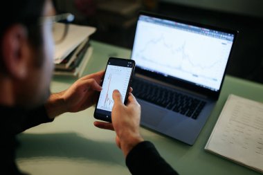 An close up shot of a traders hands using a laptop at home in the nighttime, as they track financial performance and make strategic investment decisions.