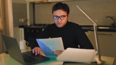 Late Night Learning E-Learning at Home with a Dedicated Student. A young Caucasian man, studying at home in the nighttime, intently focusing on his laptop for his e-learning courses.