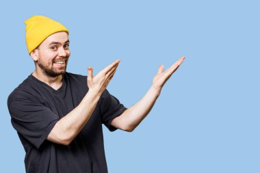 Studio shot with copy space captures an expressive and gesture man, pointing to free space, looking at the camera with a joyous expression and satisfied smile 