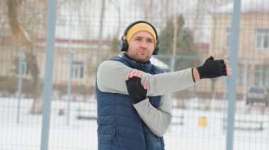 This young, fit man is seen making the most of wintertime by engaging in outdoor gymnastics exercises while wearing headphones and embodying a healthy lifestyle.