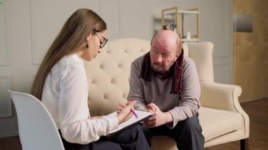 A senior man gather in a cozy living room for a psychotherapy session led by a skilled male psychologist. Seeking Understanding Senior Man in Consultation with Female Psychologist