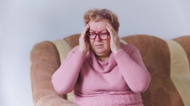 Stresli, son sınıf öğrencisi, elleriyle başını tutarak oturma odasında sürekli baş ağrısı çeken, evde migrenden muzdarip yaşlı bir kadın.