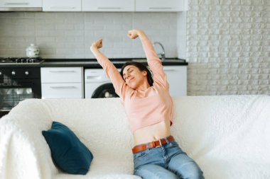 Güzel Esmer Sabah Kalkıyor, Kanepede Esniyor. Daha fazla enerji ve güç elde etmek için kollarını uzatıyorlar, mutlu bir şekilde gülümsüyorlar.