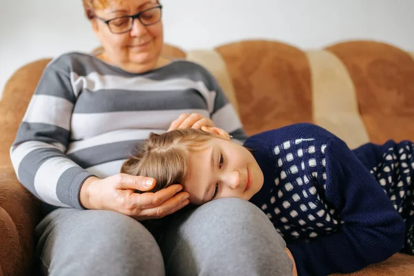 A heartwarming family portrait of a grandmother and her granddaughter sitting on the sofa hands on head, surrounded by other family members and smiling with joy and contentment.