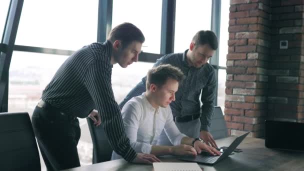 3人の男が現代のオフィススペースでノートパソコンで一緒に働いています プロの職場でラップトップとプロジェクトに協力している若い男性 — ストック動画