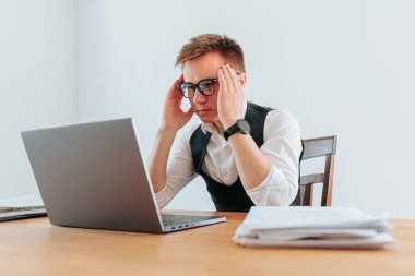 Gözlüklü bir adam bilgisayarında çalışırken yorgun ve bunalmış görünüyor. İşinin stresi ve iş yükü ile boğuşuyor. Göz yorgunluğu ve aşırı yükleme Ofis Görevinin Gerilimi