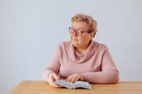 An overweight woman sitting in her cozy home, reading a book and wearing glasses that rest on the bridge of her nose, enjoying her time with a captivating read.