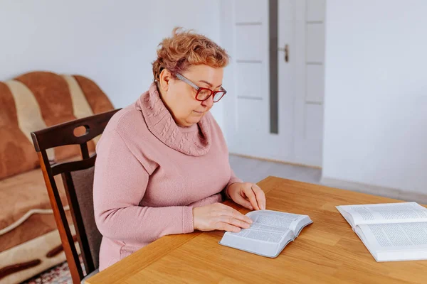 stock image An older woman, glasses on her face, sits in her home with a book in hand, the weight of the world lifting off her shoulders as she becomes lost in the story. Her glasses provide the perfect lens