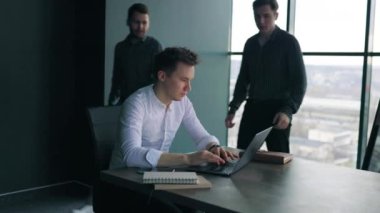 Genç bir stajyer, profesyonel bir ofiste dizüstü bilgisayarlarından yeni beceriler öğreniyor. Bir grup adam dizüstü bilgisayarlarıyla çalışıyor ve bir eğitmenle birlikte kurumsal bir eğitim veriyorlar.