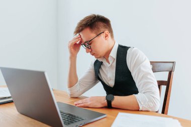 Gözlüklü bir adam başını elinde tutuyor, baş ağrısının ağırlığını ve işte geçirdiği uzun günün stresini hissediyor. Baş ağrısı ve Basınç İş Yerinin Gerilimi