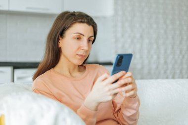 Genç bir kadın, evinde kanepede oturmuş, akıllı telefonuyla kitap okurken, huzur ve tatmin anının tadını çıkarırken yakalandı.