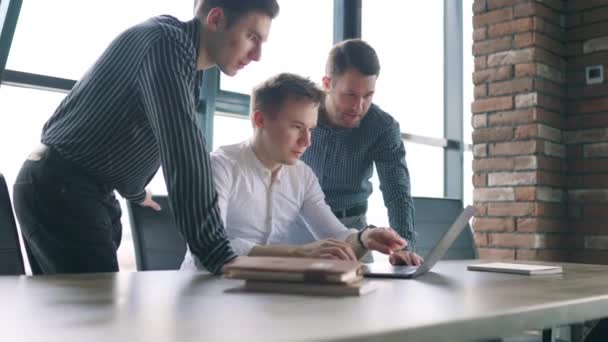 3人の若い男性がオフィスで喜んでノートパソコンで働いています オフィスでラップトップと協力している男性同僚の成功したチーム — ストック動画