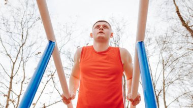 Açık hava ve Sporcu A Young Sportsmans Jimnastik Antrenmanı. Kırmızı tişörtlü genç bir atletik kaslarını dışarıda temiz havada paralel barlarda çalıştırıyor..