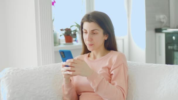 在这张照片中 一个迷人的年轻女子坐在沙发上 用智能手机浏览社交媒体 看上去既满足又快乐 — 图库视频影像
