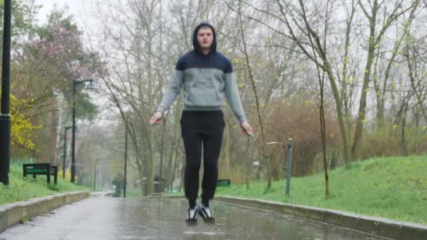 雨の日ワークアウトロープ屋外にジャンプします 若い選手は激しいジャンプロープの演習で屋外で訓練するために雨を勇敢 — ストック動画