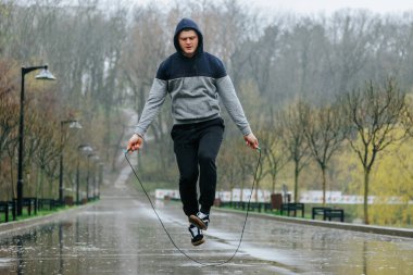 Açık hava spor salonu yağmurlu gün atlama halatı. Hava nemli olabilir, ama bu zinde genç adam hala antrenman rutinine kendini adamış durumda..