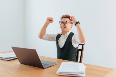 Bir ofis çalışanı, son başarısını kutlarken ellerini muzaffer bir şekilde havaya kaldırarak kabininde tek başına duruyor. Yüzündeki memnuniyet ve mutluluk ifadesi inkar edilemez..