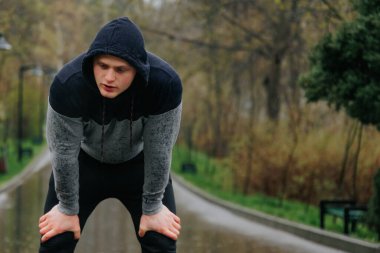 Spor yapmanın bedeli yorucu bir koşucunun dışarıda yaptığı egzersizden sonra dinlenmesidir. Açık hava eğitim yorgunluğu. Yağmurda dışarıda antrenman yaparken sınırlarını zorlayan genç bir adam..