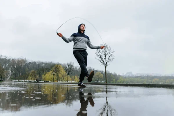 Rainy Day Gymnastics Training Jump Rope. This male athlete embraces the rain as he uses a jumping rope to build his athletic endurance during outdoor training.
