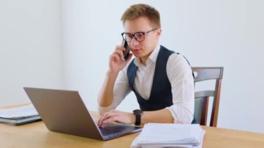 Genç bir yetişkin ofiste gündelik bir konuşma yapıyor. Bir elinde akıllı telefonunu tutarken diğer elinde dizüstü bilgisayarı var. İkisi de beyaz yakalı işçiler.