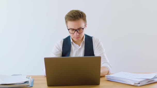 書類とノートパソコンに囲まれた自宅のオフィスで働く男性のオフィスワーカーは 仕事に集中しながら眼鏡をかけ 首にボタンを押されていない白いシャツを着ています — ストック動画