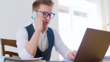 30 'lu yaşlarının başında bir adam, ofisinde oturmuş, akıllı telefonuyla patronuyla konuşuyor. Uzaktan kumandalı bir işçi ve çalışma alanı bir dizüstü bilgisayar, dosyalar ve beyaz tahtayla dolu.