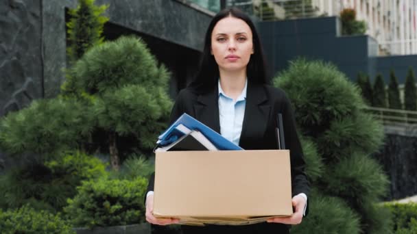 一个女人站在外面 手里拿着一个盒子 看起来迷迷糊糊的 没有工作 一个失业的失业妇女 手里拿着一盒她的东西 被解雇后妇女搬运箱子的重量 — 图库视频影像