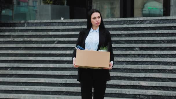 一个女人拿着一个纸盒 上面写着解雇 带着悲伤的表情走在外面 因为她失业了 — 图库视频影像
