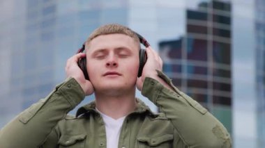 Caddede yürüyen yakışıklı bir adam, müziğinde kaybolmuş ve arka plandaki şehrin güzel mimarisinin tadını çıkarıyor. Muzik molası Genç Erkek Keyifli Müzik