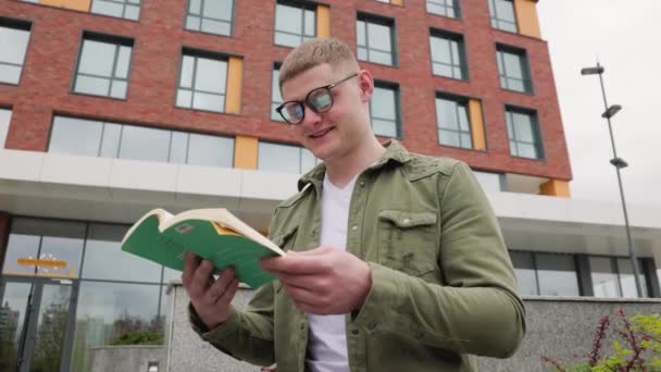 Ein Fröhlicher Junger Erwachsener Mit Brille Sitzt Mit Buch Stadtgebiet — Stockvideo