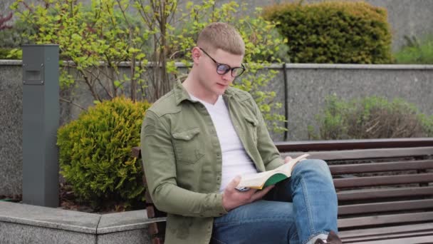 Ένα Νεαρό Αγόρι Κάθεται Έξω Διαβάζει Ένα Βιβλίο Και Χάνεται — Αρχείο Βίντεο