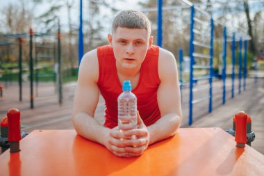 Atletik Su Şişesi Adam 'la açık hava idmanı. Atletik genç adam elinde su şişesiyle açık havada eğleniyor..